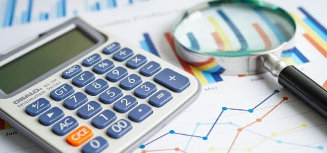 calculator sitting on graph documents with magnifying glass